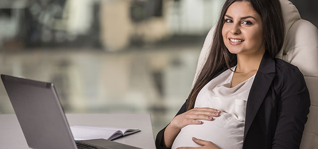 Profissional grávida, passando a mão na barriga e pensando como conciliar maternidade e carreira